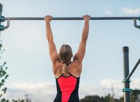 back view of a woman athlete doing pull ups on a bar outdoors. calisthenics photo