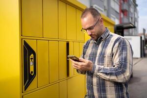 Man using smartphone at yellow delivery locker in urban area during daytime for package pickup photo