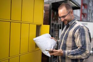 Man picks up package from secure yellow lockers in urban area after receiving notification on smartphone photo