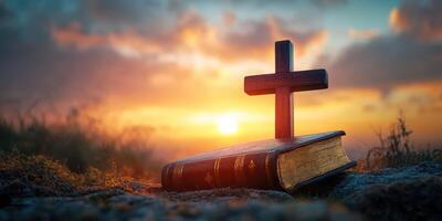 Cross and open Bible at sunset in serene landscape photo