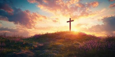 Cross standing on a hill at sunset with vibrant sky and flowers in the foreground photo