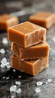 Delicious caramel squares stacked with sea salt on a dark surface photo