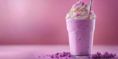Delicious whipped cream topped purple milkshake served in a tall glass with a striped straw against a pink background photo