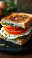 Deliciously stacked sandwich with fried egg, fresh vegetables, and herbs on a black plate photo
