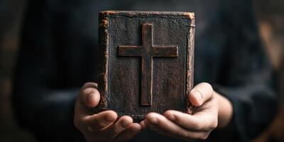 A person holding a weathered book with a cross symbol in a dimly lit space, conveying a sense of reverence and spirituality photo
