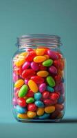 Colorful jelly beans fill a clear glass jar against a vibrant blue background, showcasing an assortment of sweets in a playful display photo