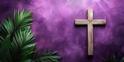 Wooden cross against a purple wall with green palm leaves in a religious setting photo