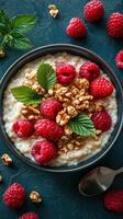 Creamy oatmeal topped with fresh raspberries and walnuts in a dark bowl on textured surface photo