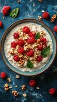 Healthy oatmeal topped with fresh raspberries, granola, and mint leaves served in a bowl on a blue textured surface photo