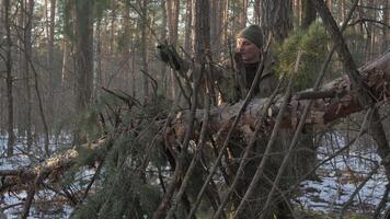 Man Building a Survival Shelter in Winter Forest, A man constructs a bushcraft shelter using branches and pine in a snowy forest. video