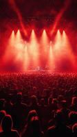 Concert under vibrant red lights featuring a lively audience and a performing band on stage photo