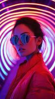 Young woman poses in stylish sunglasses against vibrant neon lights in an urban setting at night photo