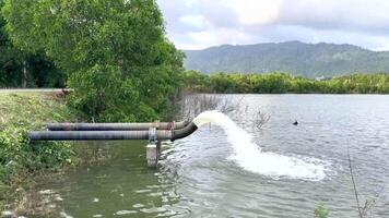 Water flows from a large metal pipe into a natural reservoir as part of an irrigation system. This illustrates water management, drainage, and sustainable agriculture solutions video