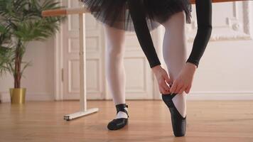 Ballerina puts on pointe shoes on leg in dance class. Classical ballet dancer woman in dance studio. Ballerina putting on tying classical pointe shoes for dance training. Ballet school concept video