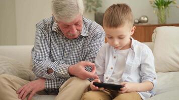 Happy family at home. Old senior man grandfather boy grandson enjoying time together watching on phone. Good time at home. grandparent and child together. Older generation modern tech usage video