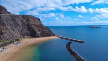 Aerial view of Las Teresitas Beach in San Andres, Tenerife, featuring golden sand, palm trees, and serene waters under an overcast sky. video