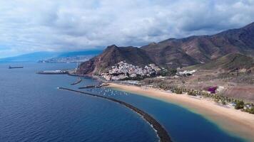 Aerial panoramic view of Las Teresitas Beach in San Andres, Tenerife, Canary Islands, with golden sand, palm trees, and calm waters under a cloudy sky video
