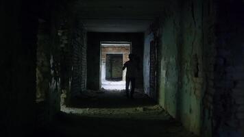 Desolate corridor revealing man wandering through abandoned building, waving hands with haunting sense of despair and isolation within shadowy, decaying urban environment video