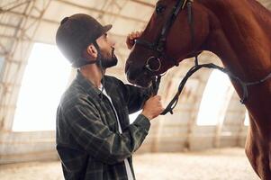 Taking ,care of animal. Young man with a horse is in the hangar photo
