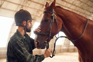 Standing, and holding animal. Young man with a horse is in the hangar photo