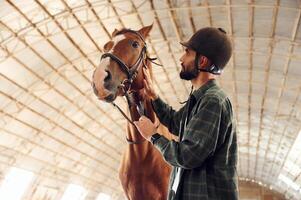 Standing together. Young man with ,a horse is in the hangar photo