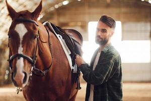 Installing ,the saddle.. Young man with a horse is in the hangar photo