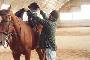 Installing the saddle.. Young man with a horse is in the hangar photo