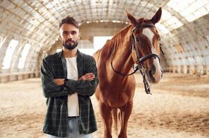 Front view.. Young man with a horse is in the hangar,. photo