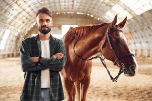 Front view. Young, man with a horse is in the hangar photo