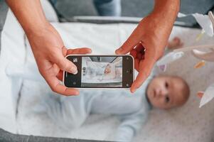 Taking picture by ,smartphone. Father with his newborn baby is indoors. Conception of single dad photo