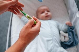 Holding, thermometer, kid in the cradle.. Father with his newborn baby is indoors. Conception of single dad photo