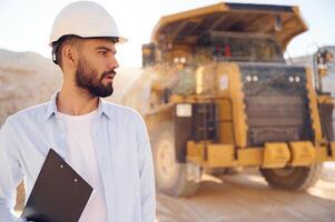 Beautiful man in uniform, is working in the quarry at daytime. With haul truck photo