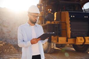 In hard hat,, eyewear and with notepad. Man in uniform is working in the quarry at daytime photo