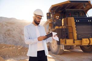 In, hard hat, eyewear and with notepad. Man in uniform is working in the quarry at daytime photo