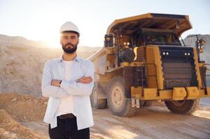 Standing against big haul truck. Man in uniform ,is working in the quarry at daytime photo
