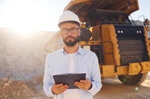 In hard hat,. eyewear and with notepad. Man in uniform is working in the quarry at daytime photo