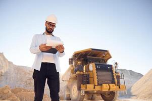 Smart person is with documents in hands.. Man in uniform is working in the quarry at daytime photo