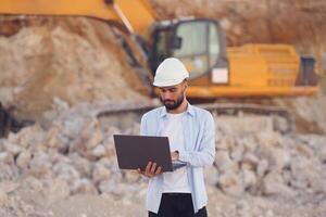 With laptop. Man in uniform is working in the quarry at daytime. photo