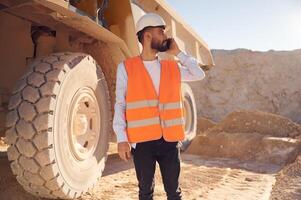 Using smartphone. Man, in ,uniform is working in the quarry at daytime photo