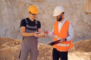 Holding and showing rock, that is in the hand. Two men in uniform are working together in the quarry photo