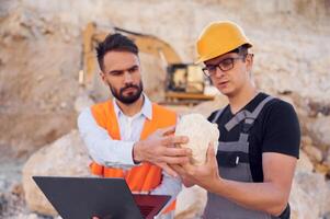 Checking rock, that, is in the hands. Two men in uniform are working together in the quarry photo