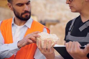 Checking ,rock that is in the hands. Two men in uniform are working together in the quarry photo