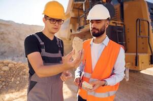 Checking rock that is in the hands.. Two men in uniform are working together in the quarry photo