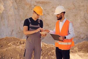 Holding ,and showing rock that is in the hand. Two men in uniform are working together in the quarry photo
