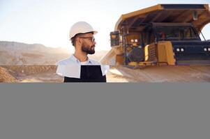 In hard hat, eyewear and with notepad. Man in uniform is working in the quarry at daytime photo