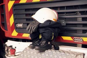 Close up view of ,firefighter's hat, gloves, jacket, pants and shoes. With big vehicle photo