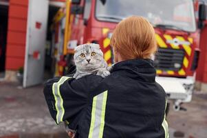 View from behind. Holding cat on shoulders. Woman firefighter in uniform is at work in department photo