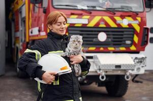 Conception of savior. Holding cat in hands. Woman firefighter in uniform is at work in department photo