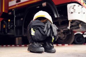 Close ,up view of firefighter's hat, gloves, jacket, pants and shoes. With big vehicle photo