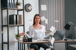 Throwing stickers, up into air. Young beautiful woman in white clothes is in the office photo